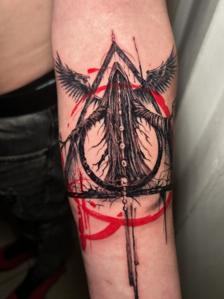 Tatuaggio trash polka di Lenny Fastidio, simbolo triangolare con ali sull'avambraccio