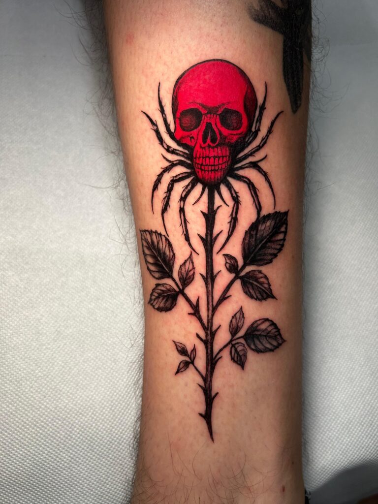 Tatuaggio di Lenny Fastidio, teschio rosso e rose sull'avambraccio